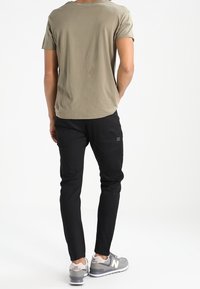 Olivově zelené tričko s krátkým rukávem, černé slim-fit kalhoty a šedé tenisky. Jednoduchý design s kulatým výstřihem a bez viditelných vzorů.