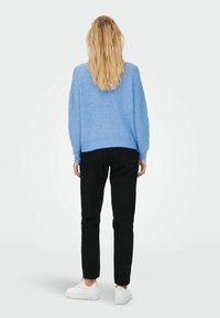 Suéter de punto azul claro con un corte relajado, combinado con pantalones negros y zapatillas blancas, visto desde atrás sobre un fondo neutral.