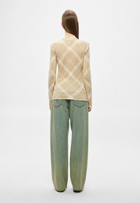 Top mulat cu mâneci lungi, croială strâmtă, în nuanță de bej, cu un model în formă de diamant. Pantaloni largi și lejeri din denim bleu deschis, cu talie medie și buzunare la spate.