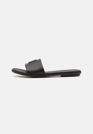 Sort flad slide sandal med bredt læderrem og let hævet hæl på ensfarvet hvid baggrund.