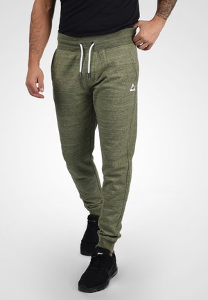 Jogging en vert olive avec une finition texturée, taille élastique, cordons blancs et accents latéraux ; assortis à des baskets noires.