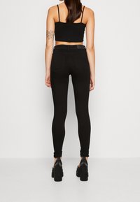 Jeans ajustados negros de cintura alta con una textura suave, combinados con un top corto negro ajustado. La modelo lleva tacones de plataforma negros.