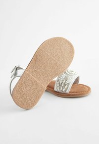 Vitrande vit sandal med silverremmar, mockautsole och texturerad gummisula. Har dekorativ beading på ovansidan.