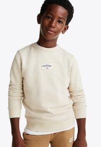 Felpa beige con scollatura rotonda e polsini a coste. Presenta una toppa rettangolare con il testo "Tommy HILFIGER". Tessuto morbido.