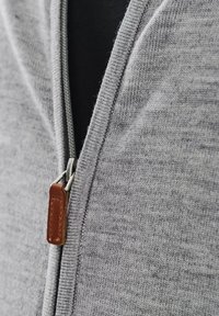 Szary dziergany kardigan zapinany na zamek z teksturowanej tkaniny, z metalowym zamkiem błyskawicznym i skórzaną pętelką w kolorze brązowym. Dopasowany dekolt, bez wzoru.