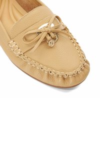 Mocassin en cuir tan avec un nœud décoratif, un accent en métal doré et un détail tressé sur le bord. Bout arrondi doux avec une semelle flexible.