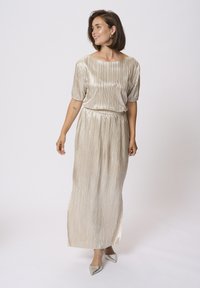 Robe maxi en or métallisé avec texture plissée, manches courtes bouffantes et taille cintrée, assortie à des chaussures argentées à bout pointu.