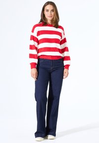Rood en wit gestreepte gebreide trui met een ronde hals, gecombineerd met donkerblauwe flare jeans en lichtgekleurde sneakers.