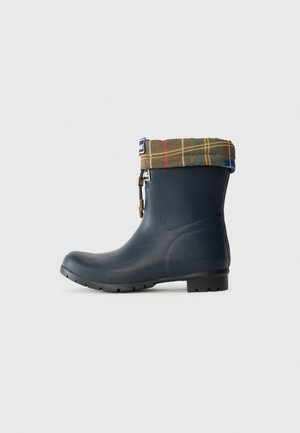 Navy rubber rain boots with a tartan fabric cuff in brown, green, and red. Features textured sole and adjustable hardware detail.