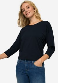 Námořnická modrá, dlouhý rukáv, top s kulatým výstřihem a volným střihem, spárovaný s modrými džínami. Měkká tkanina s hladkým povrchem a minimálním designem.