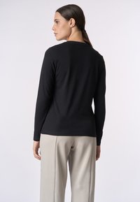Top nero a maniche lunghe, forma aderente, texture morbida, scollatura rotonda, abbinato a pantaloni beige chiaro a gamba larga, che mostrano un design semplice.