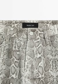 Gros plan sur un pantalon imprimé serpent gris et blanc avec fermeture par bouton et étiquette noire Massimo Dutti à la ceinture.