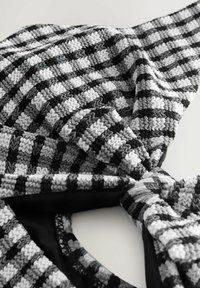 Svart och vit rutig tyg med strukturerade, upphöjda zickzackmönster, knutna i ena änden; mjukt, stretchy material med en slät insida.