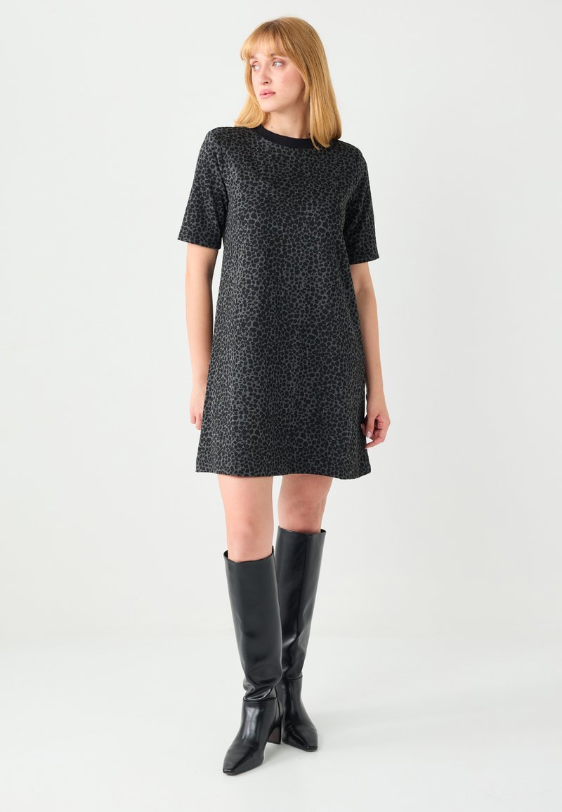 Robe à imprimé léopard noir avec manches courtes, présentant une coupe décontractée et un ourlet droit, associée à des bottes noires brillantes montant jusqu'au genou.