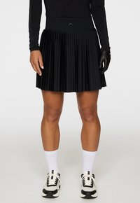 Mustaselkäinen, pleatattu hame, jossa on korkea vyötärö. Valmistettu kevyestä materiaalista, jossa on terävät pleatit ja hillitty logoteema vyötäröllä.