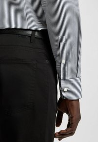 Randig skjortan i svart och vitt, med standardkrage, knappmanchetter och en skräddarsydd passform, tillsammans med svarta byxor.