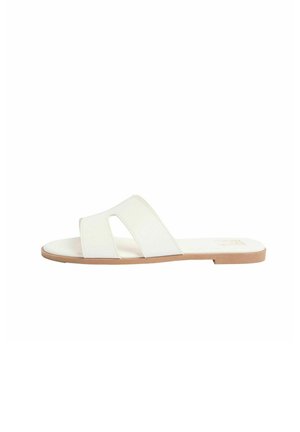 White flat slide sandal with wide cut-out strap and tan sole, designed for casual wear.