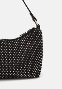 Sac à épaule noir avec des clous en argent recouvrant sa surface, fermeture éclair et fine sangle attachée par un anneau en métal.