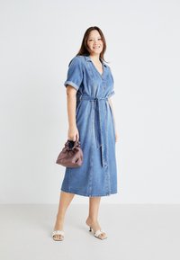 Denim-mekko, jossa on lyhyet käännetyt hihat, V-pääntie ja vyötäröhihna. Eteen on ommeltu nappeja ja se ulottuu polven puoliväliin. Yhdistetty pieneen, rentoon ruskeaan laukkuun.