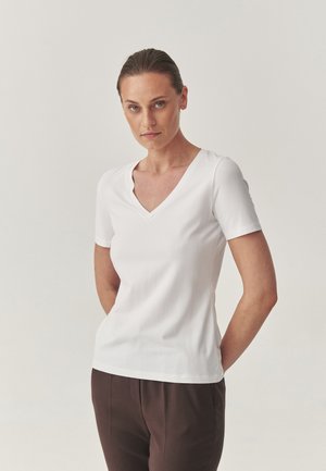 Witte short-sleeve V-hals T-shirt van zachte katoen, nauwsluitend ontwerp, gladde textuur, gecombineerd met donkerbruine broeken.