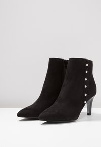 Black suede ankle boots with a pointed toe, tapered heel, and a side zipper. Features decorative pearl-like studs along the outer side.