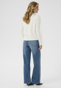 Witte gebreide trui met een ontspannen pasvorm, gecombineerd met mid-blauwe wijdeman jeans. De trui heeft een geribde zoom en manchetten.