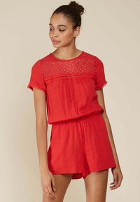 Rompers rouge à manches courtes, présentant un motif géométrique au niveau de l'empiècement, une taille élastique et un tissu texturé.