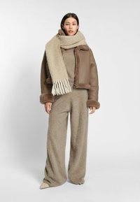 Brun läderjacka i kort modell med fårskinnsdetaljer, beige ullblandad tröja och vida byxor, kombinerat med en fransad beige scarf.