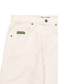 Pantalones de lona color beige que presentan un parche de logo verde y negro en el bolsillo trasero, cierre de botón y diseño estándar de cinco bolsillos.