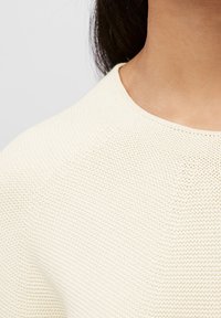 Cremfarbener Strickpullover mit rundem Ausschnitt. Die Textur ist weich, mit einem subtilen Muster und einer glatten Oberfläche.
