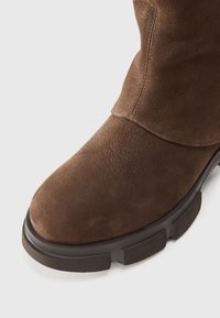 Brown suede ankle boot with a rounded toe, a slightly slouched upper, and a textured rubber sole. Minimal stitching detail.