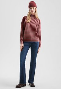 Bordeaux gestreepte langed raglan turtleneck trui, gecombineerd met donkerblauwe uitlopende jeans en bruine instappers. Een gebreide beanie maakt de outfit compleet.