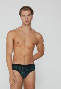 Männerbriefs mit kariertem Muster in den Farben Grün, Schwarz und Blau, mit einem einfarbigen schwarzen Bund und einer glatten Stofftextur.