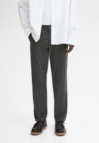 Dark gray, tailored trousers with a straight fit, two side pockets, and a button closure. Worn with a white shirt and brown lace-up shoes.
