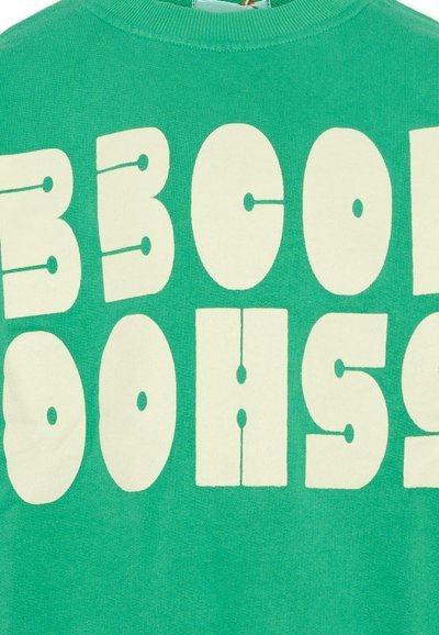 Felpa verde con grandi lettere color crema che formano la scritta "BE COOL NO NOISE" in un carattere audace e arrotondato sul petto.