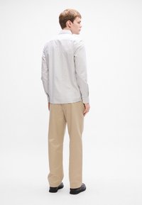Gestreepte, lange mouwen shirt in wit en grijs, gedragen met beige broeken. Heeft een klassieke kraag en knopen bij de mouwen. Zwarte schoenen zichtbaar.
