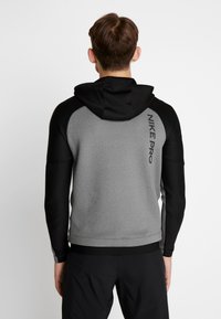 Hombre vestido con una sudadera con capucha de Nike Pro en gris y negro, vista desde atrás, con el texto "NIKE PRO" en la parte superior derecha.