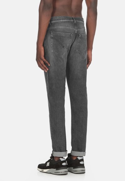 Jeans in denim grigio con vestibilità dritta, caratterizzati da una fila singola di cuciture a vista, cinque tasche e orli arrotolati. Indossati con sneakers nere.