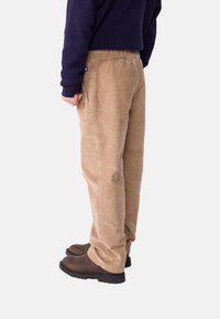 Pantaloni in corduroy color sabbia con vita elasticizzata, tasche laterali e vestibilità comoda, abbinati a stivali marroni e una maglia blu navy.