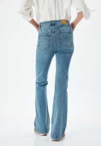 Jeans de tiro alto y pernera acampanada en denim azul claro con un lavado desgastado. Presenta dos bolsillos traseros y una etiqueta de cuero en la cintura.