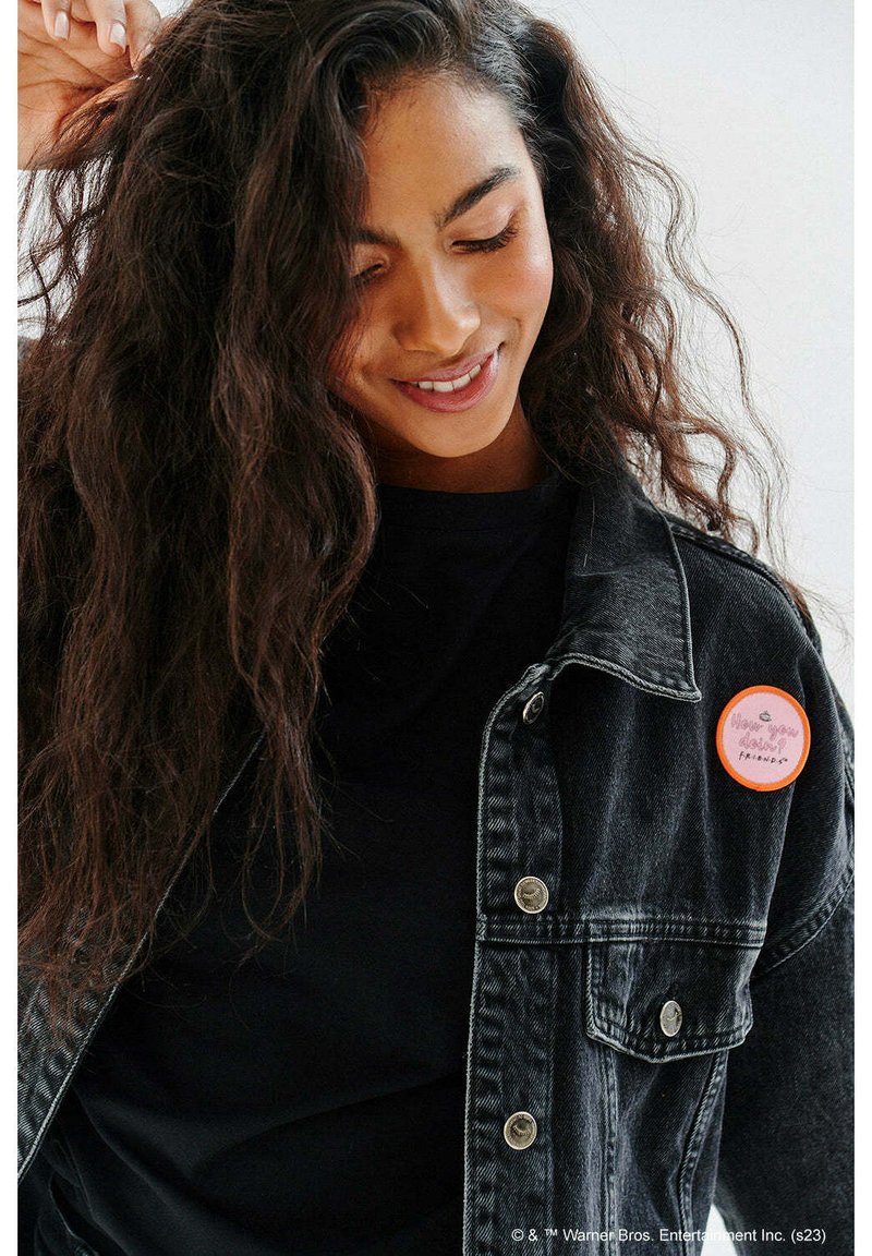 Czarna dżinsowa kurtka z srebrnymi guzikami, noszona na czarnej koszuli. Posiada okrągły pomarańczowy przypinek na klapie z napisem "Jak leci? Przyjaciele."