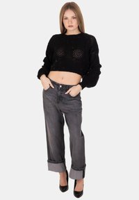 Maglione cropped nero a maglia con vestibilità morbida, abbinato a jeans grigi a vita alta arrotolati alla caviglia e tacchi neri.