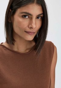 Bruine mouwloze top met een textuur gebreide ontwerp. Heeft een ronde halslijn en subtiele stiksels, tegen een lichte achtergrond.