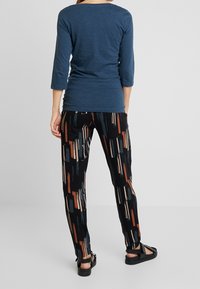 Modrá dlouhá tričko s rukávem, které je kombinováno s černými kalhotami s abstraktními štětci v barvách rezavé a krémové. Černé sandály dokončují outfit.