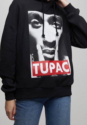 Zwarte hoodie met een grote zwart-witte gezichtsprint en de naam "TUPAC" in dikke witte letters op een rode achtergrond aan de voorkant.