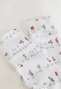 Chaussettes blanches ornées de motifs festifs de décorations de Noël, y compris des cadeaux, du houx, des cannes en sucre et des sapins, posées à plat.