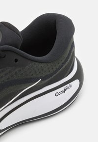 Zwarte en olijfgroene mesh sneaker met een gewatteerde kraag, gebogen witte en zwarte zool, en "ComfiRide" branding op de hiel.