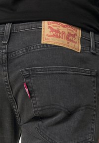 Primer plano de un bolsillo trasero de unos jeans negros con una etiqueta de cuero de marca y una etiqueta de tela roja en la costura del bolsillo.
