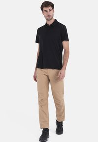 Zwarte poloshirt met korte mouwen en een kraag, gecombineerd met lichtbeige cargobroek met zakken en een ontspannen pasvorm. Zwarte sneakers maken de look compleet.