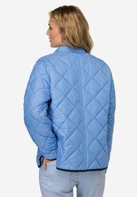 Světle modrá prošívaná bunda s diamantovým vzorem, která má hladkou texturu, stojatý límec a černé lemy na spodním okraji a manžetách.